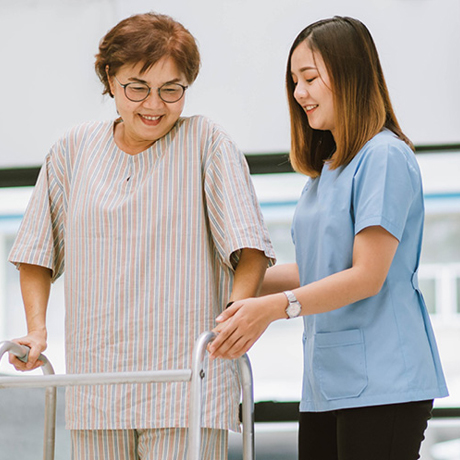 Nurse helping older woman to do walking therapy.