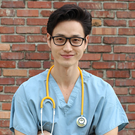 Male clinician standing outside in-front of brick wall.