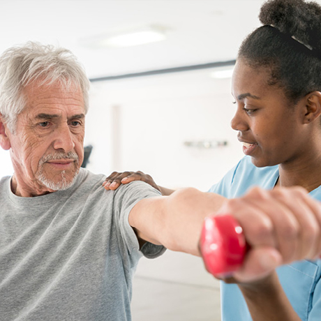 Female nurse is helping an older male to do physical therapy.