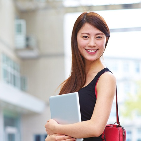 Woman holding laptop with red bag standing outdoor.